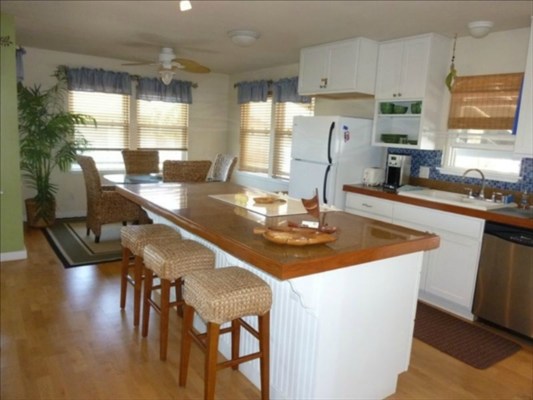 8325 Elepaio Road Kekaha, HI 96752 - Photo 4 of 10 a kitchen with stainless steel appliances granite countertop a sink dishwasher a stove a refrigerator a dining table and chairs with wooden floor