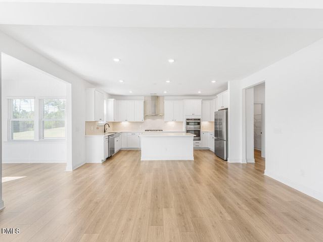 a view of empty room with wooden floor and kitchen view