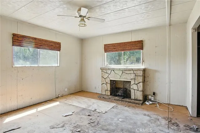 an empty room with windows fireplace and fan