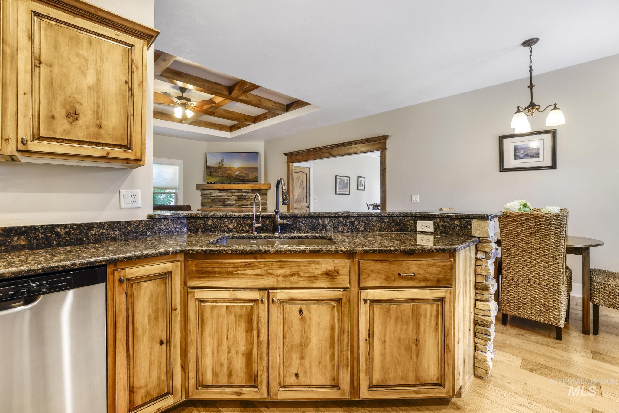 2157 Cayuse Street Twin Falls, ID 83301 - Photo 12 of 48 Kitchen featuring stainless steel dishwasher, coffered ceiling, brown cabinetry, hanging light fixtures, and dark stone counters
