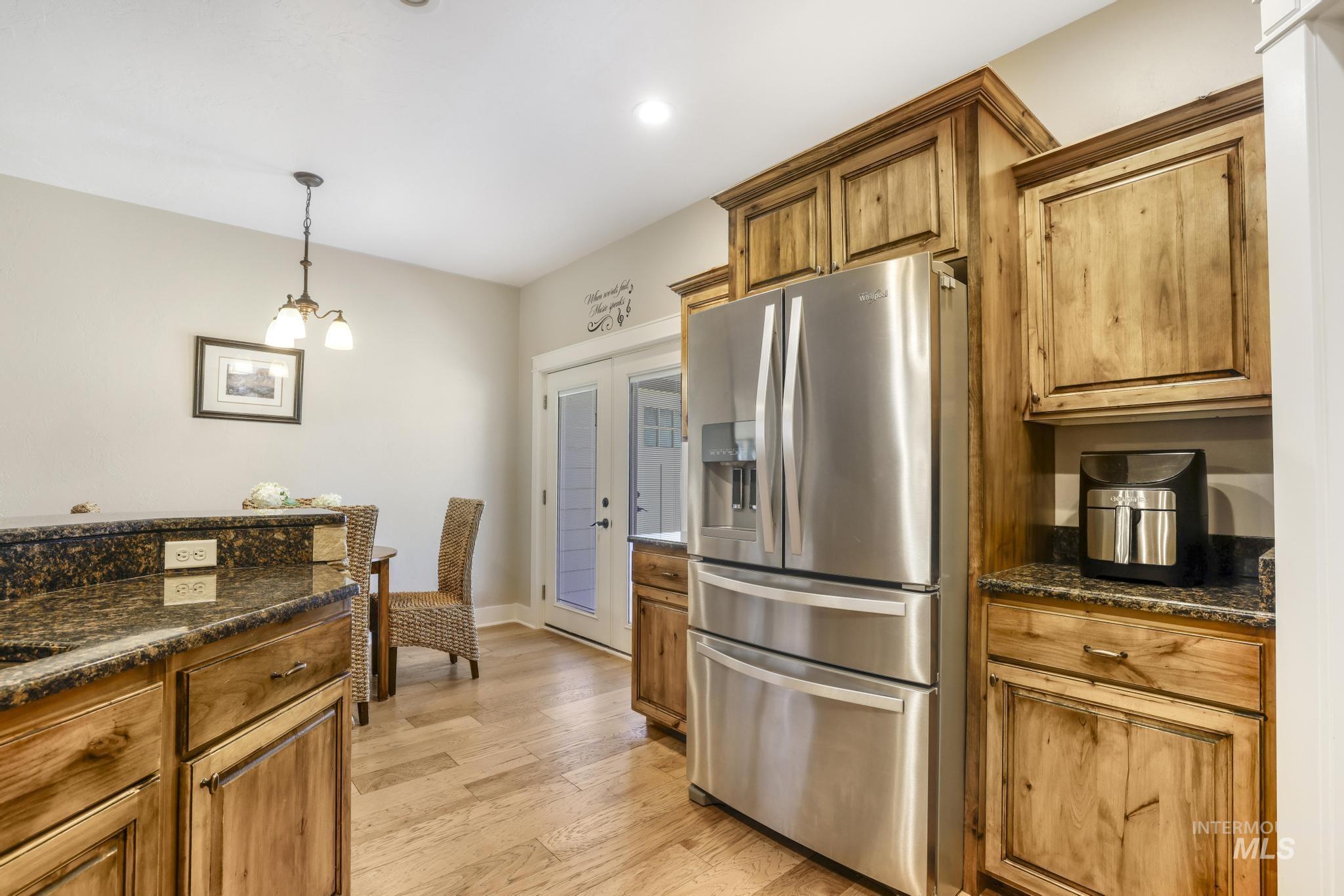 2157 Cayuse Street Twin Falls, ID 83301 - Photo 13 of 48 Kitchen with stainless steel refrigerator with ice dispenser, dark stone counters, brown cabinets, hanging light fixtures, and light wood-type flooring