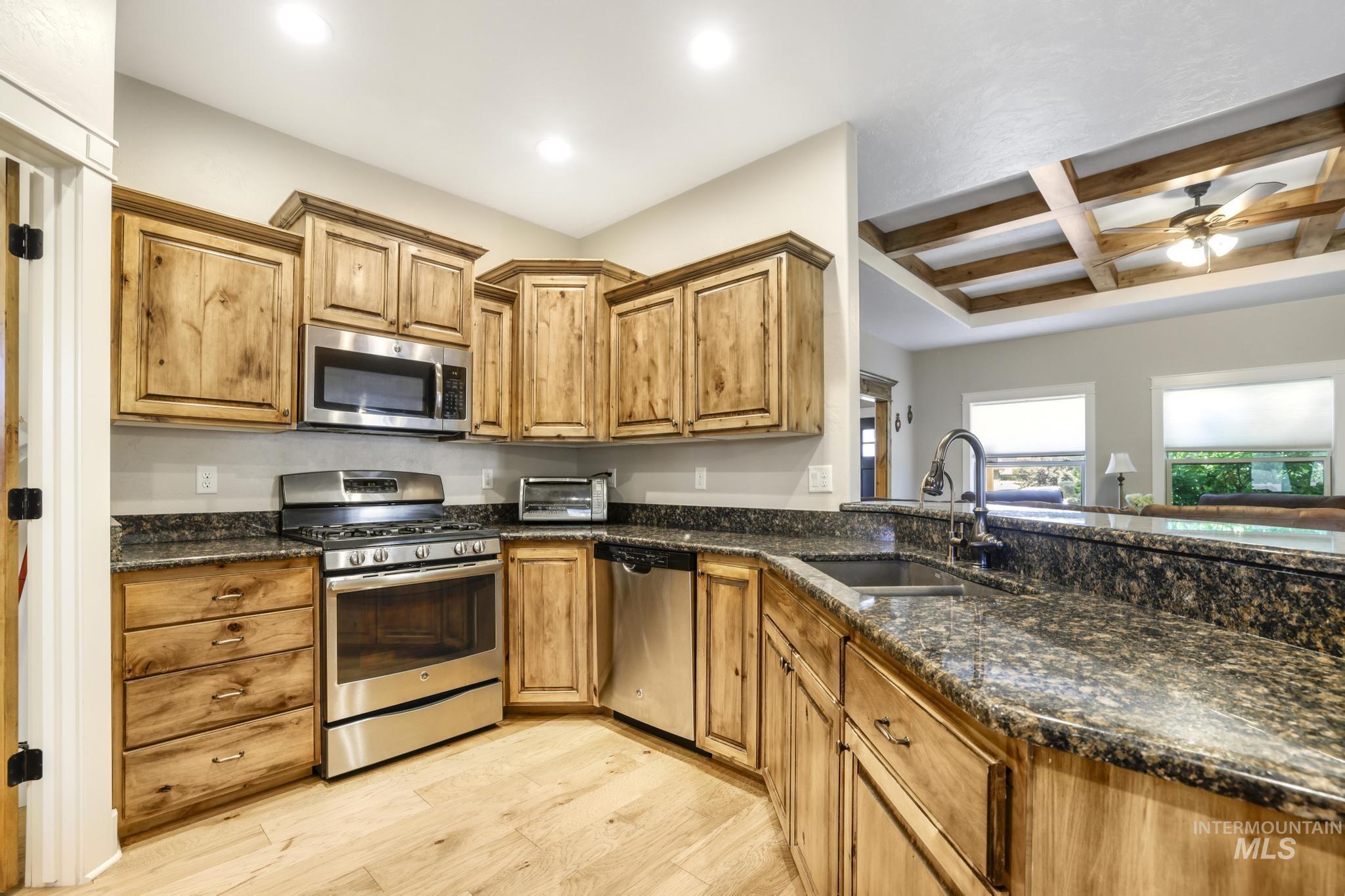 2157 Cayuse Street Twin Falls, ID 83301 - Photo 9 of 48 Kitchen featuring coffered ceiling, stainless steel appliances, dark stone countertops, beamed ceiling, and light wood finished floors