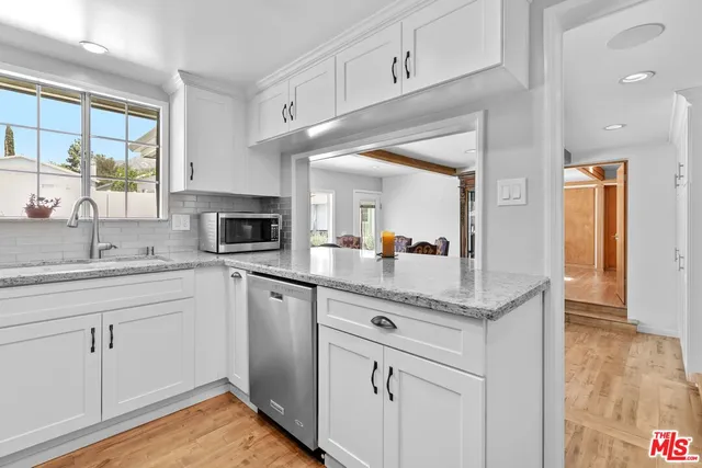 a kitchen with granite countertop a sink stainless steel appliances white cabinets and wooden floor