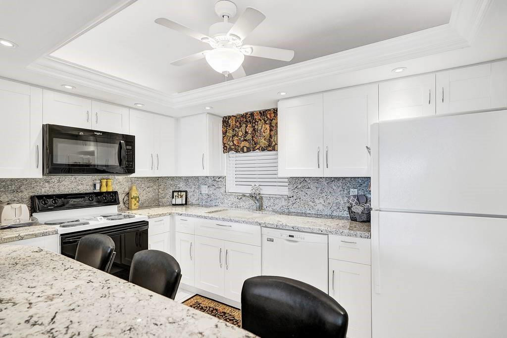 303 North Riverside Drive, Unit 503 Pompano Beach, FL 33062 - Photo 8 of 29 a kitchen with a sink a stove a microwave oven a refrigerator with white cabinets and wooden floor