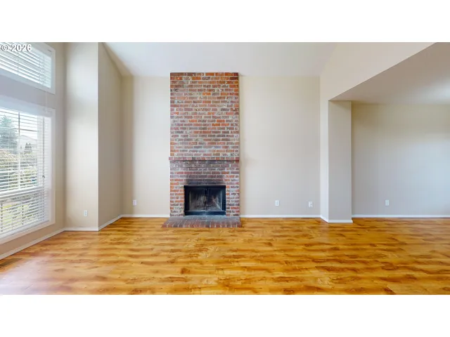 a view of an empty room with wooden floor and a fireplace