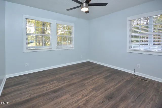 an empty room with wooden floor ceiling fan and windows