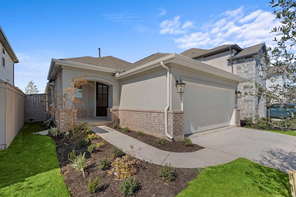 View of front facade with driveway, brick siding, an attached garage, stucco siding, and roof with shingles