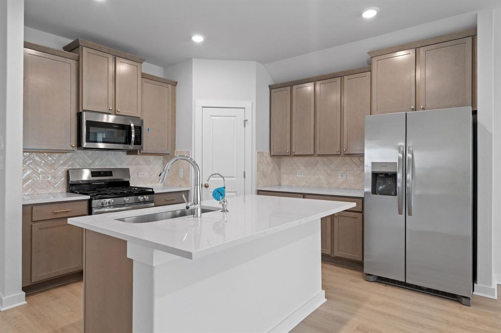 212 Brandywine Road Hutto, TX 78634 - Photo 3 of 35 Kitchen featuring stainless steel appliances, an island with sink, light wood finished floors, light stone countertops, and tasteful backsplash