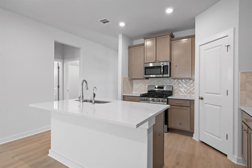 212 Brandywine Road Hutto, TX 78634 - Photo 4 of 35 Kitchen featuring a center island with sink, appliances with stainless steel finishes, light stone counters, decorative backsplash, and light wood-type flooring