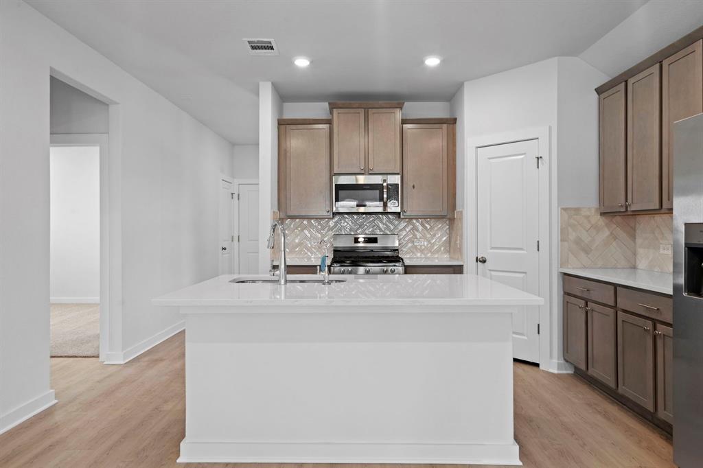 212 Brandywine Road Hutto, TX 78634 - Photo 5 of 35 Kitchen featuring appliances with stainless steel finishes, an island with sink, backsplash, light stone counters, and recessed lighting