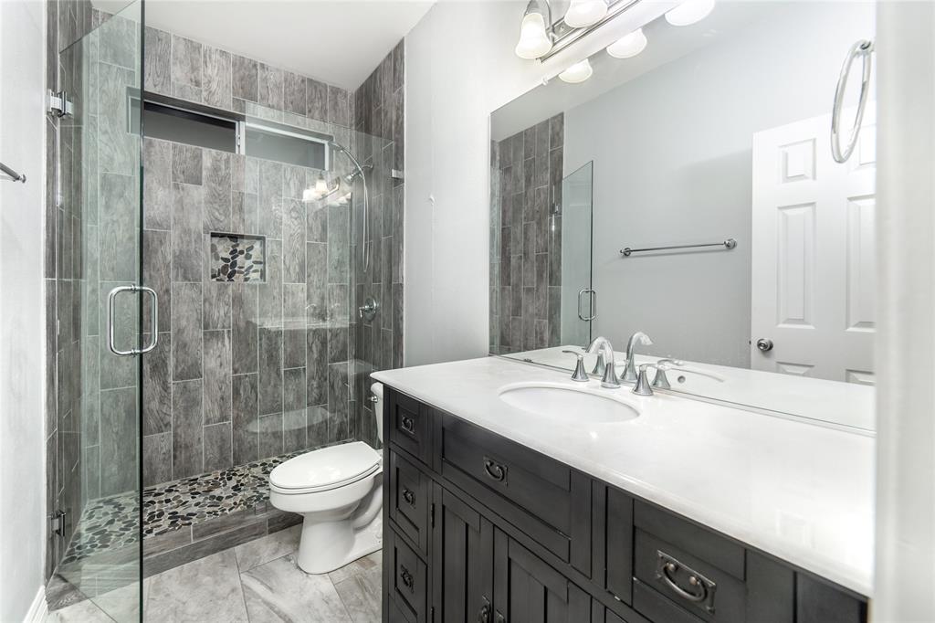 5801 Yeary Road Plano, TX 75093 - Photo 16 of 33 Modern bathroom with a glass-enclosed shower featuring gray wood-finish wall tile, a mosaic stone shower floor, and a built-in shower niche