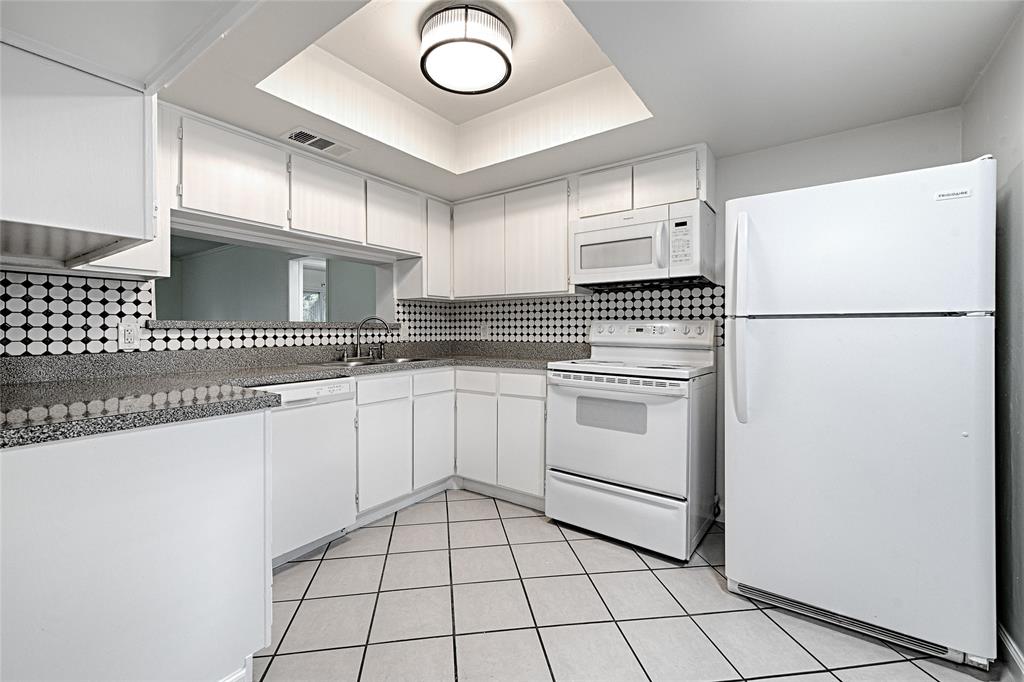 4561 North O'Connor Road, Unit 1292 Irving, TX 75062 - Photo 3 of 10 White kitchen featuring extensive cabinetry, tile flooring, granite-style countertops, and a full suite of white appliances including a refrigerator, range, microwave, and dishwasher