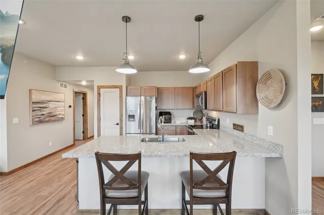 a kitchen with stainless steel appliances granite countertop a refrigerator a sink dishwasher a stove a dining table and chairs with wooden floor