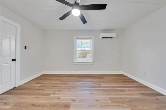 an empty room with wooden floor ceiling fan and windows