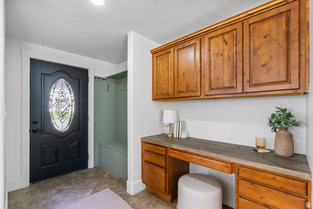 432 Calnette Drive Sandy, UT 84070 - Photo 14 of 48 Entryway featuring a decorative glass-insert door, built-in mudroom bench, custom wood cabinetry, integrated desk space, and tile flooring