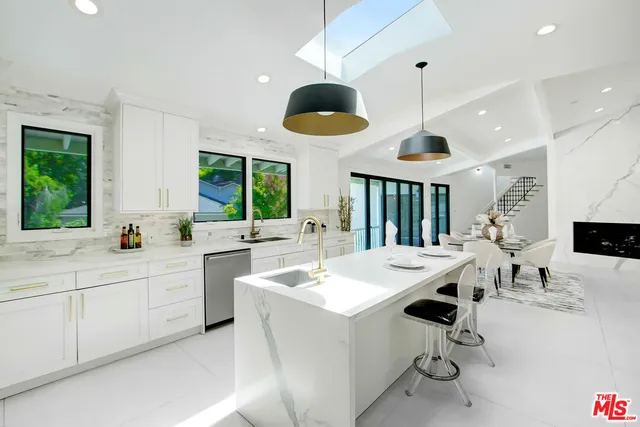 a large white kitchen with a white center island a stove a refrigerator and a view of living room