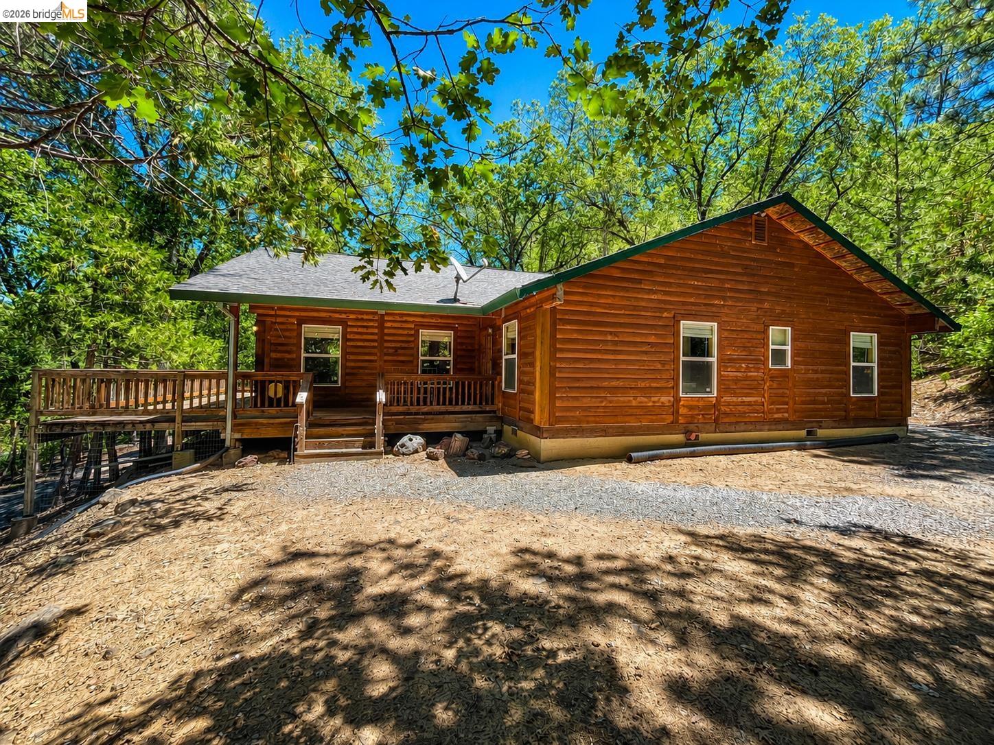 21181 Phoenix Lake Road Sonora, CA 95370 - Photo 3 of 34 Log cabin exterior with an expansive wooden deck, featuring a green roof and white-framed windows