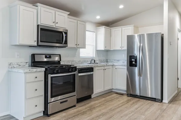 a kitchen with stainless steel appliances white cabinets a sink a stove a microwave and cabinetry