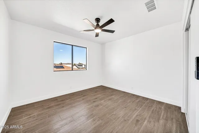 an empty room with wooden floor ceiling fan and windows