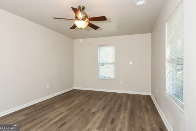an empty room with wooden floor fan and windows