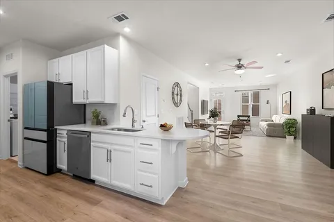 a kitchen with stainless steel appliances a refrigerator a stove a sink dishwasher and white cabinets with wooden floor