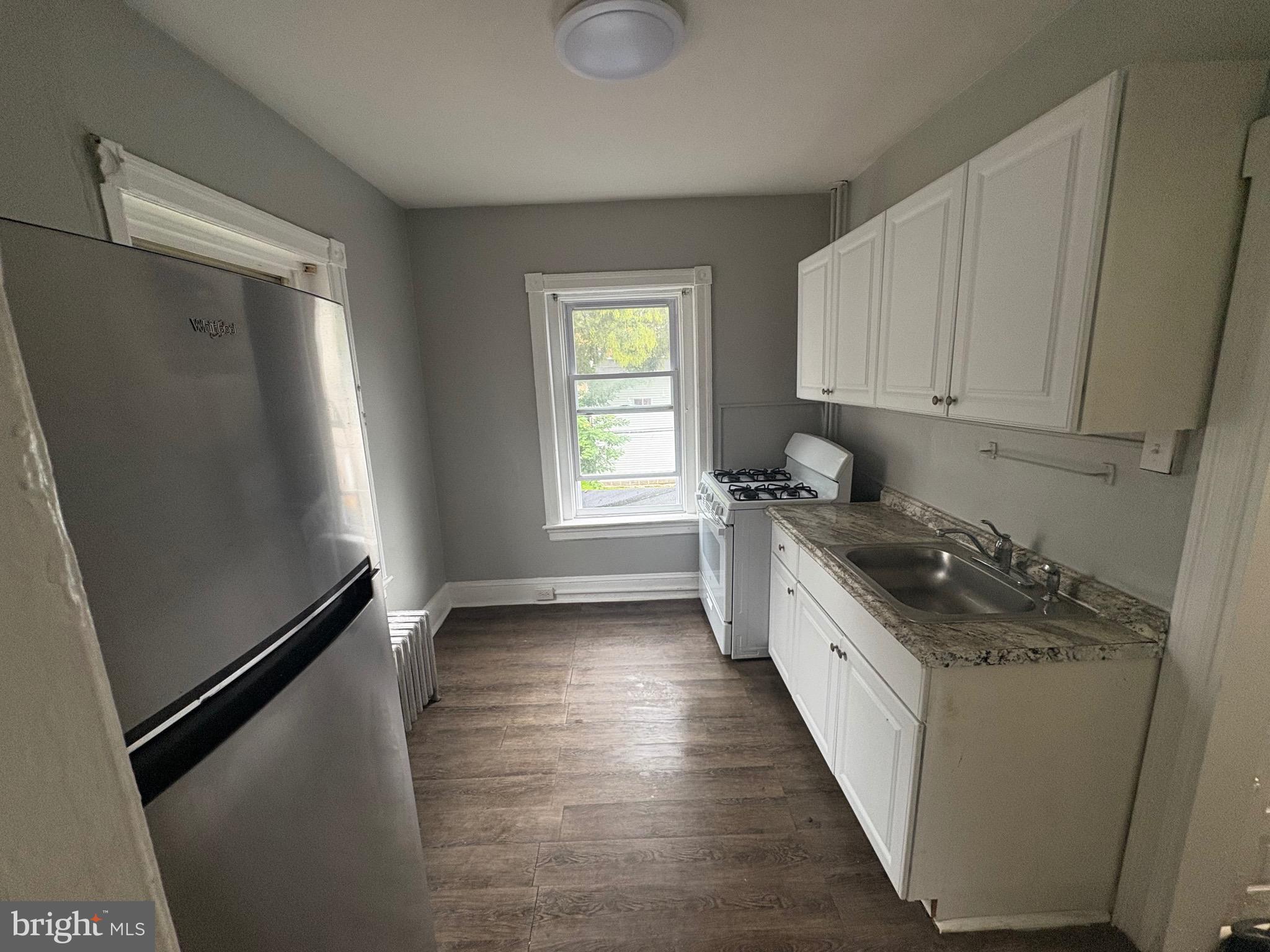 1337 71st Avenue, Unit 2 Philadelphia, PA 19126 - Photo 7 of 16 a kitchen with granite countertop a refrigerator a sink a stove and white cabinets