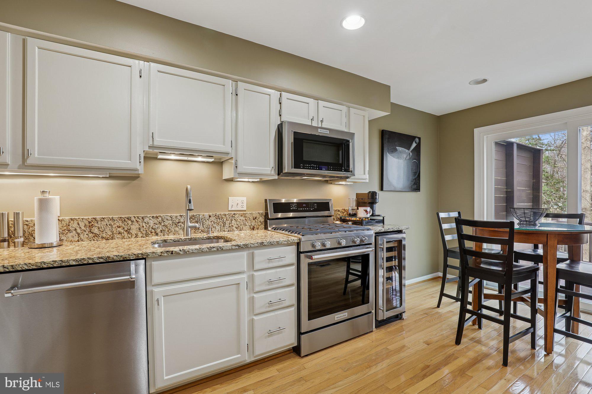 8019 Galla Knoll Circle Springfield, VA 22153 - Photo 13 of 57 a kitchen with stainless steel appliances granite countertop a stove top oven a sink dishwasher a dining table and chairs with wooden floors