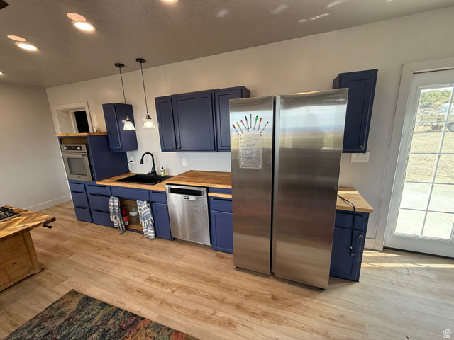14183 High Mesa Loop Duchesne, UT 84021 - Photo 36 of 56 Kitchen featuring blue cabinets, stainless steel appliances, wooden counters, light wood-style flooring, and hanging light fixtures