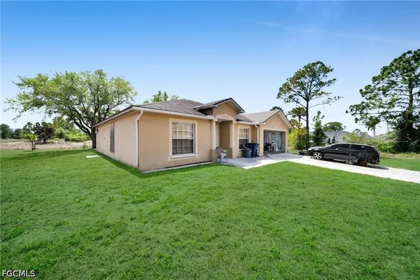 a view of a white house in front of a big yard with large trees