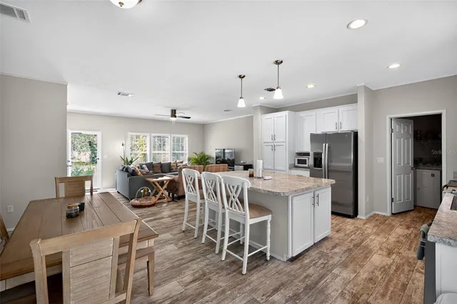 a kitchen with stainless steel appliances kitchen island granite countertop a refrigerator oven a sink a dining table and chairs with wooden floor