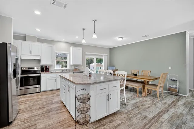 a kitchen with stainless steel appliances granite countertop a table chairs wooden floors and a view of living room