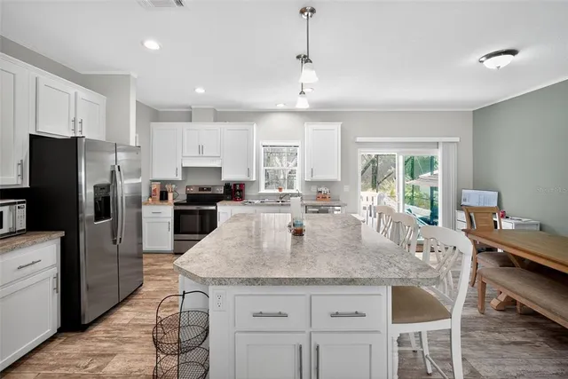 a kitchen with stainless steel appliances granite countertop a stove a refrigerator a sink a dining table and chairs