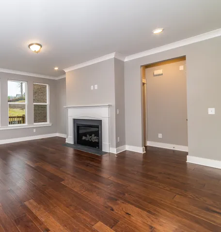 a view of an empty room with wooden floor fireplace and a window