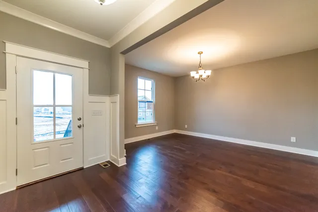 an empty room with wooden floor chandelier and windows