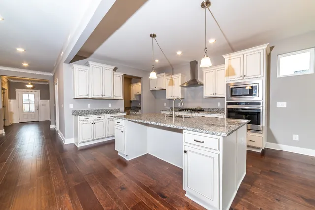 a large kitchen with granite countertop a large stove a sink dishwasher a refrigerator and white cabinets with wooden floor