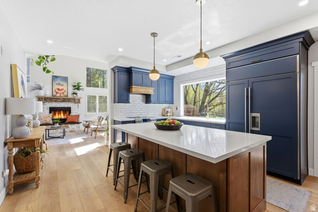 7935 Mustang Loop Road Park City, UT 84098 - Photo 19 of 60 Open-concept kitchen and living area featuring custom blue cabinetry, wood-finish flooring, a stone fireplace, a large kitchen island with a light-toned countertop, and a built-in refrigerator