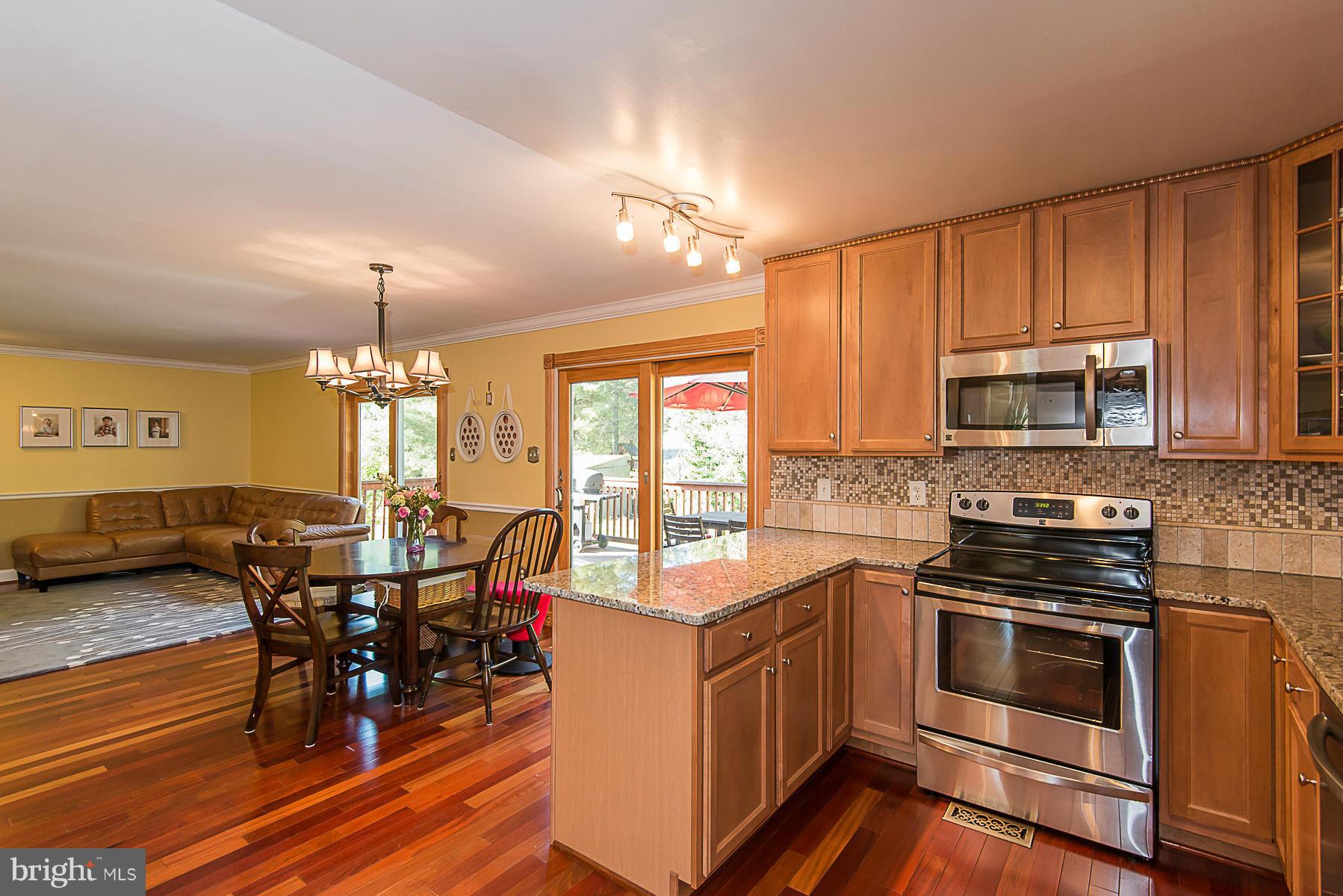 4050 Macalpine Road Ellicott City, MD 21042 - Photo 11 of 30 a kitchen with stainless steel appliances kitchen island granite countertop a stove top oven a dining table and chairs with wooden floor