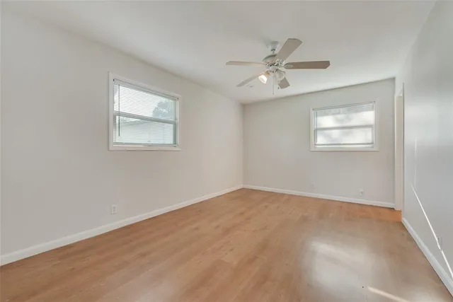 an empty room with wooden floor ceiling fan and windows