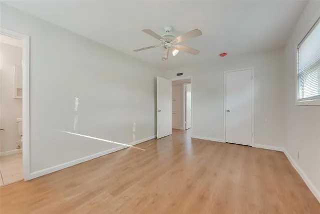 an empty room with wooden floor fan and windows