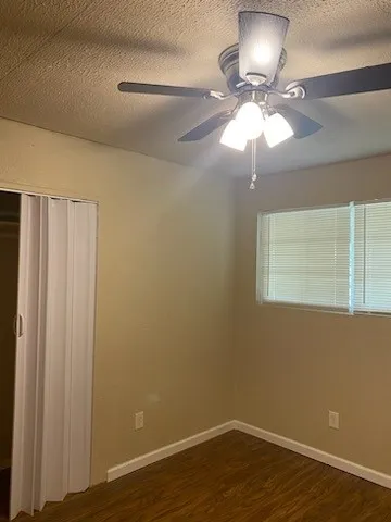 a view of an empty room with wooden floor and a fan