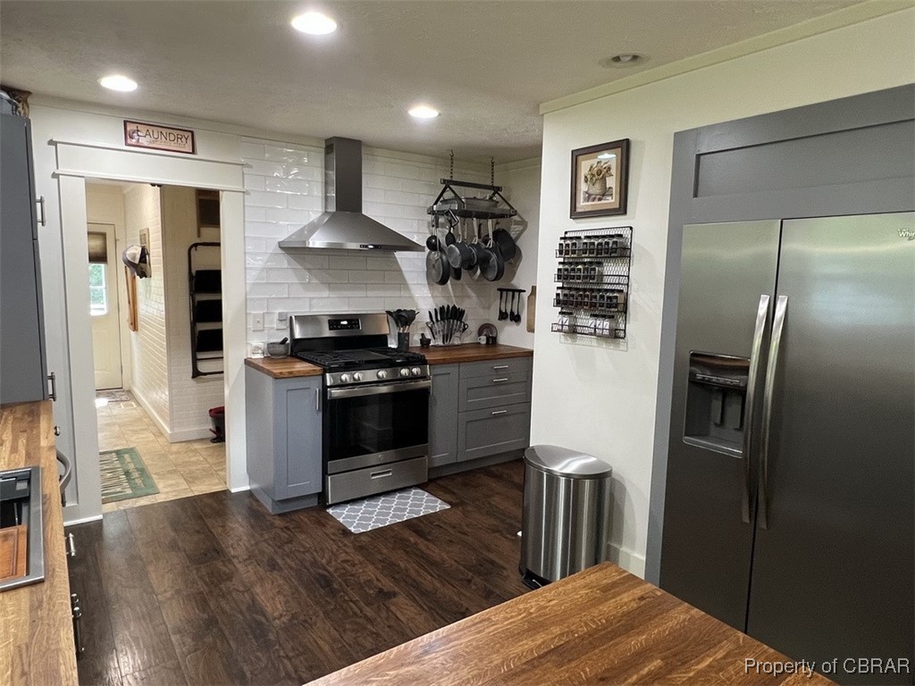 102 Mechams Cove Road Topping, VA 23169 - Photo 20 of 40 Kitchen with butcher block countertops, stainless steel appliances, wall chimney range hood, gray cabinets, and dark wood-type flooring