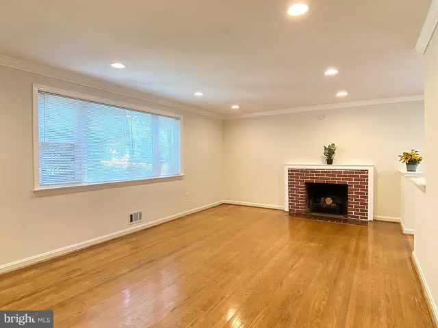 a view of an empty room with wooden floor fireplace and a window