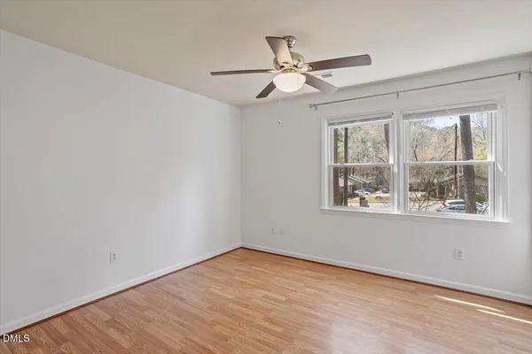 an empty room with wooden floor fan and windows