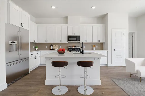 a kitchen with stainless steel appliances granite countertop a refrigerator a stove a sink and chairs with wooden floor