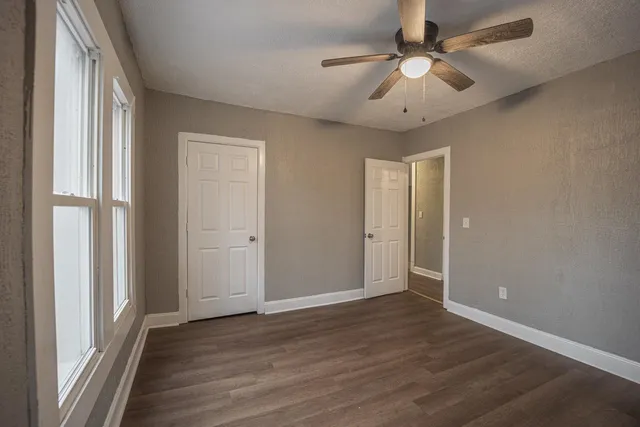 an empty room with wooden floor fan and windows