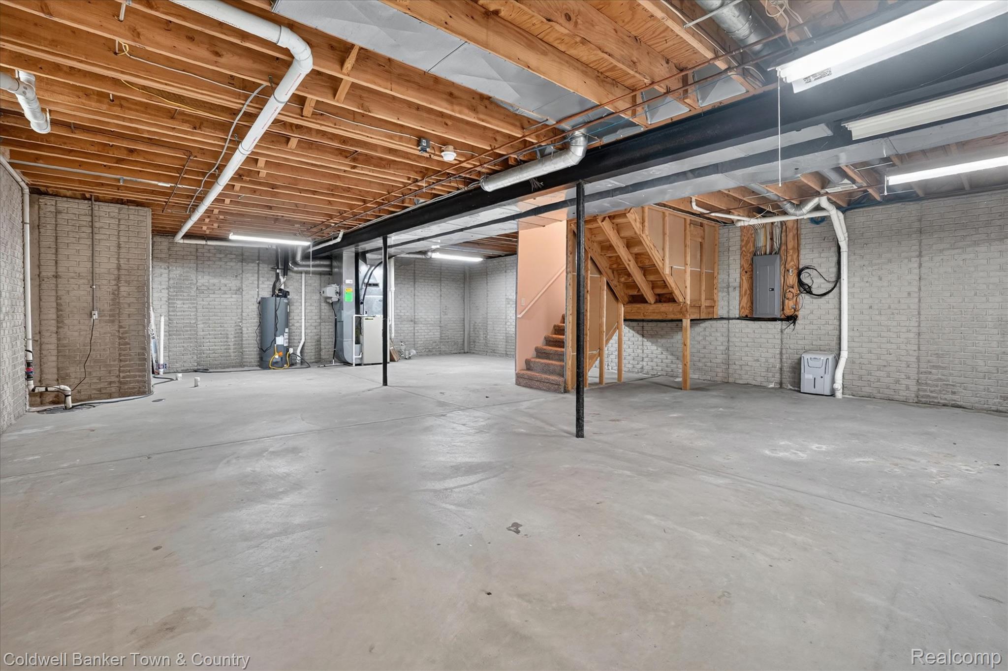 1725 Town Commons Drive Howell, MI 48855 - Photo 47 of 53 Unfinished basement featuring expansive concrete flooring, exposed wood joists, block foundation walls, and a built-in wooden staircase