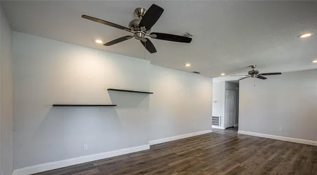 a view of an empty room with wooden floor and a ceiling fan