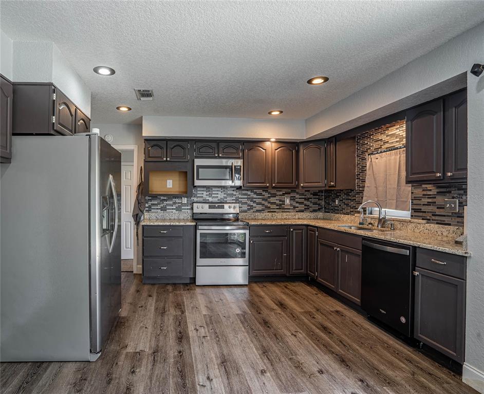 2814 William Lane Lakeland, FL 33812 - Photo 8 of 18 a kitchen with stainless steel appliances kitchen island granite countertop a refrigerator a sink dishwasher a stove with wooden cabinets and floor