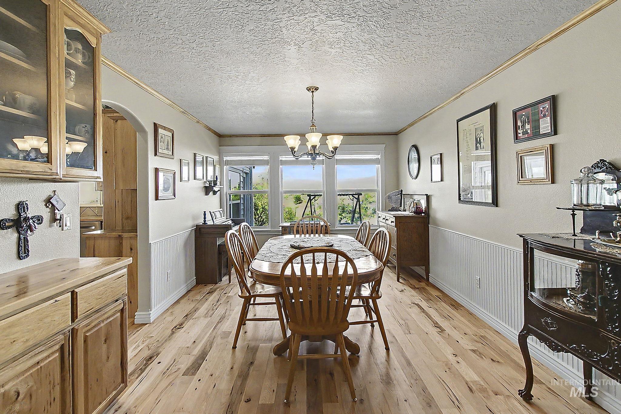 6900 West Charters Lane Melba, ID 83641 - Photo 17 of 49 Dining area featuring wood-finish flooring, wainscoting, and a multi-light chandelier