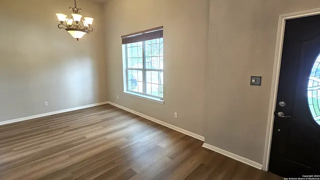 an empty room with wooden floor chandelier fan and windows
